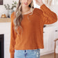 Woman wearing a rust-colored sweater and blue jeans in a home setting