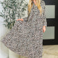 Woman wearing a leopard print dress standing indoors with decorative elements.